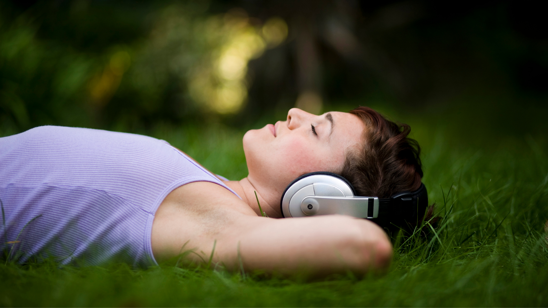 woman lying on grass with hands behind head wearing headphones